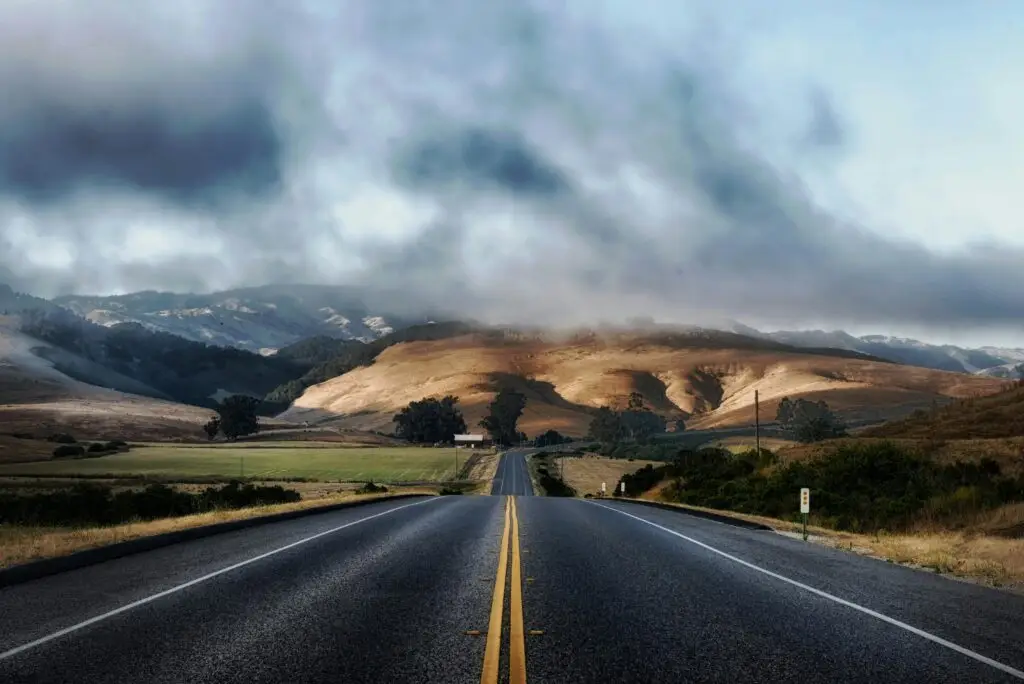 Dramatic sky over a deserted highway flanked by rolling hills, ideal for travel themes.